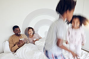Mother, father and children jump on bed in morning for playing together, fun and quality time at home. Love, black
