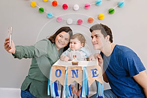 Mother father dad taking selfie with child kid toddler. Caucasian family with baby boy celebrating first birthday at home. Cupcake