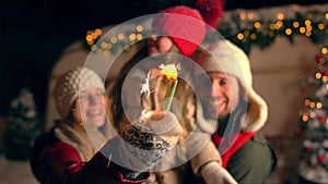 Mother, father, daughter holding sparklers at Christmas eve snowing weather.