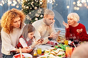 Mother, father, daughter sitting with smartphone near granny