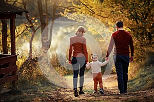 Mother father and daughter are walking along the forest path three and around the trees with yellow leaves