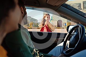 Mother and father dropping off daughter in front of school, girl turning back to parents sitting in car and smiling