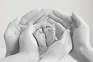 mother and father gently hold the babys foot in their hands. Black and white image with soft focus on the babys leg