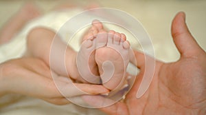 Mother and father hold newborn baby bare feet. Tiny feet in woman hand. Cozy morning at home. Love and family concept.