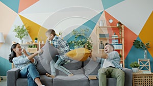 Mother, father and kid fighting pillows having fun together on sofa in house