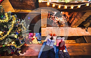 Mother father and kids sitting at cosy fireplace on winter time - Lovely family resting together on woolen socks at home fire