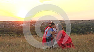 mother and father kiss and hug little child sunset, playing superheroes dressed red cloaks, happy family, brave savior