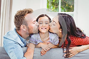 Mother and father kissing daughter at home