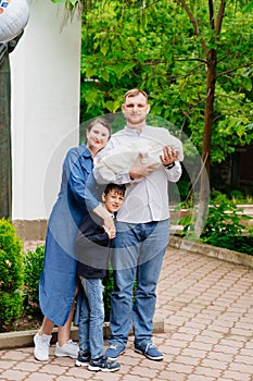 mother and father with newborn baby and eldest child stands at exits of hospital