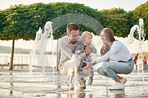 Mother and father are playing with their son in the fountains in the park