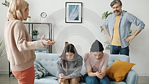 Mother and father punishing teenage children yelling and gesturing while kids sitting on couch feeling guilty