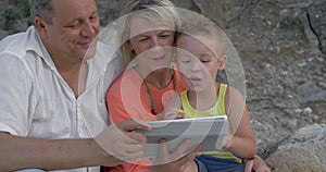 Mother,father and son watching video on pad while sitting on beach