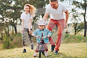 Mother and father teaching daughter how to ride bicycle outdoors