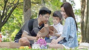 Mother and father are teaching kid in park with book.Happy family picnic concept