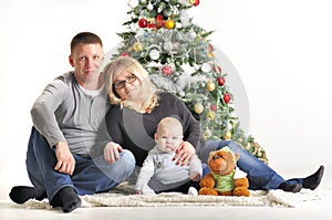 Mother, the father and their small child sits near Christmas tree