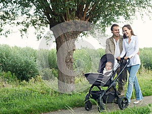 Mother and father walking outdoors and pushing baby in pram