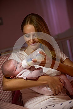 Mother Feeding Baby With Bottle In Nursery