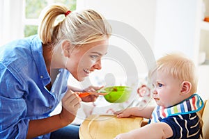 Mother Feeding Baby Boy In High Chair