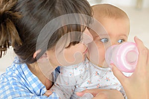 mother feeding baby boy with milk bottle at home