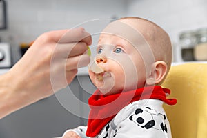 Mother is feeding baby boy with spoon. Healthy baby food at home