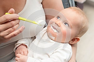 mother feeding baby boy with white yogurt, baby looking at mum