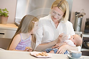 Mother feeding baby with daughter eating