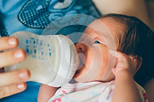 Mother feeding baby girl with nutrition in a bottle.