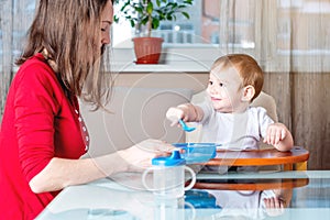 Mother feeding the baby holding hand with a spoon of food. Healthy baby nutrition. The emotions of a child while eating