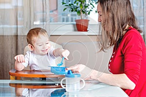 Mother feeding the baby holding hand with a spoon of food. Healthy baby nutrition. The emotions of a child while eating