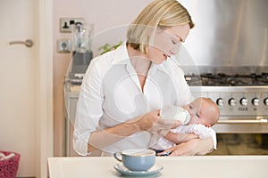 Mother feeding baby in kitchen with coffee