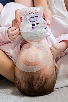 Mother feeding baby with milk bottle in living room