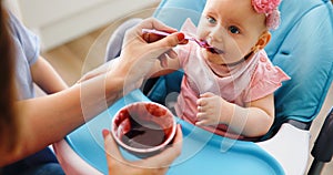 Mother feeding baby with spoon indoors