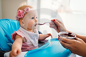 Mother feeding baby with spoon indoors