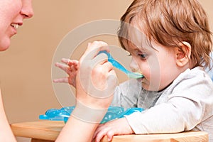 Mother feeding baby with a spoon at the table.