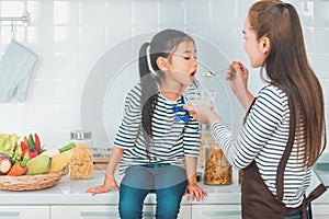 Mother feeding child with cereal on kitchen counter for breakfast with vegetable and ingredient on background