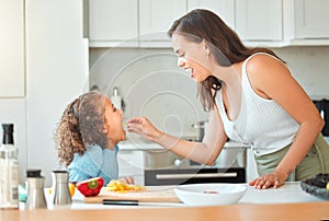 Mother feeding child vegetables while cooking together in the kitchen. Mom telling daughter to open wide and eat her