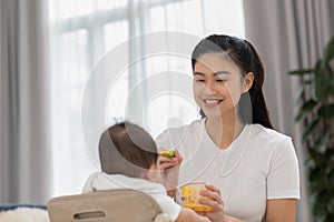 Mother feeding her asian baby daughter with pumpkin mashed or vegetable mash for vitamin on rubber spoon.Mom trying feed little