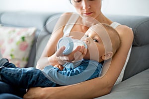 Mother, feeding her baby boy from bottle, sitting on the couch a