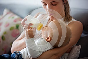 Mother, feeding her baby boy from bottle, sitting on the couch a