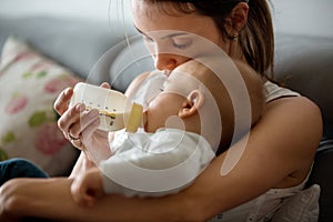 Mother, feeding her baby boy from bottle, sitting on the couch a