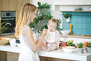 Mother Feeding Her Baby Girl with a Spoon. Mother Giving Food to her Child at Home. Baby food