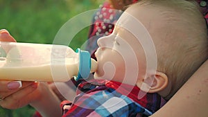 Mother feeding her baby son with a bottle of milk on the outdoor.