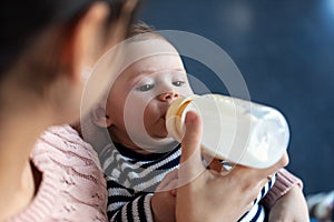 Mother feeding her baby son with feeding bottle while sitting on sofa at home