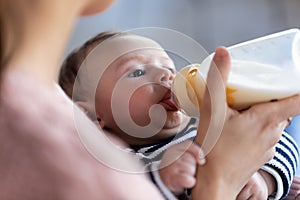 Mother feeding her baby son with feeding bottle while sitting on sofa at home