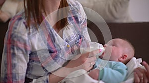 Mother feeding her baby son from milk bottle, holding him in hands