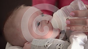 Mother feeding her baby son from milk bottle, holding him in hands, closeup detail