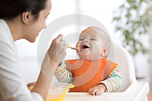 Mother feeding her baby with spoon. Mother giving healthy food to her adorable child at home photo