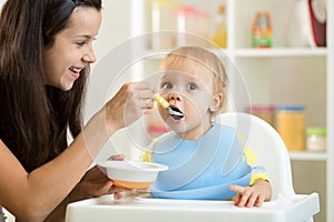 Mother feeding her baby with spoon. Mother giving healthy food to her adorable child at home