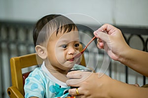 Mother feeding her baby with spoon. Mother giving healthy food to her adorable child at home.