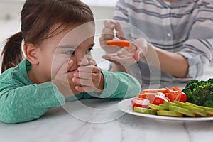 Mother feeding her daughter indoors, closeup. Little girl refusing to eat vegetables